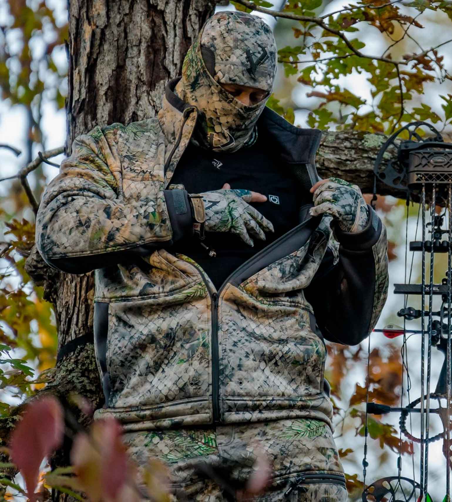 Bowhunter in a treestand wearing a Vycah Oculus Heated Vest under camo while pulling up a bow