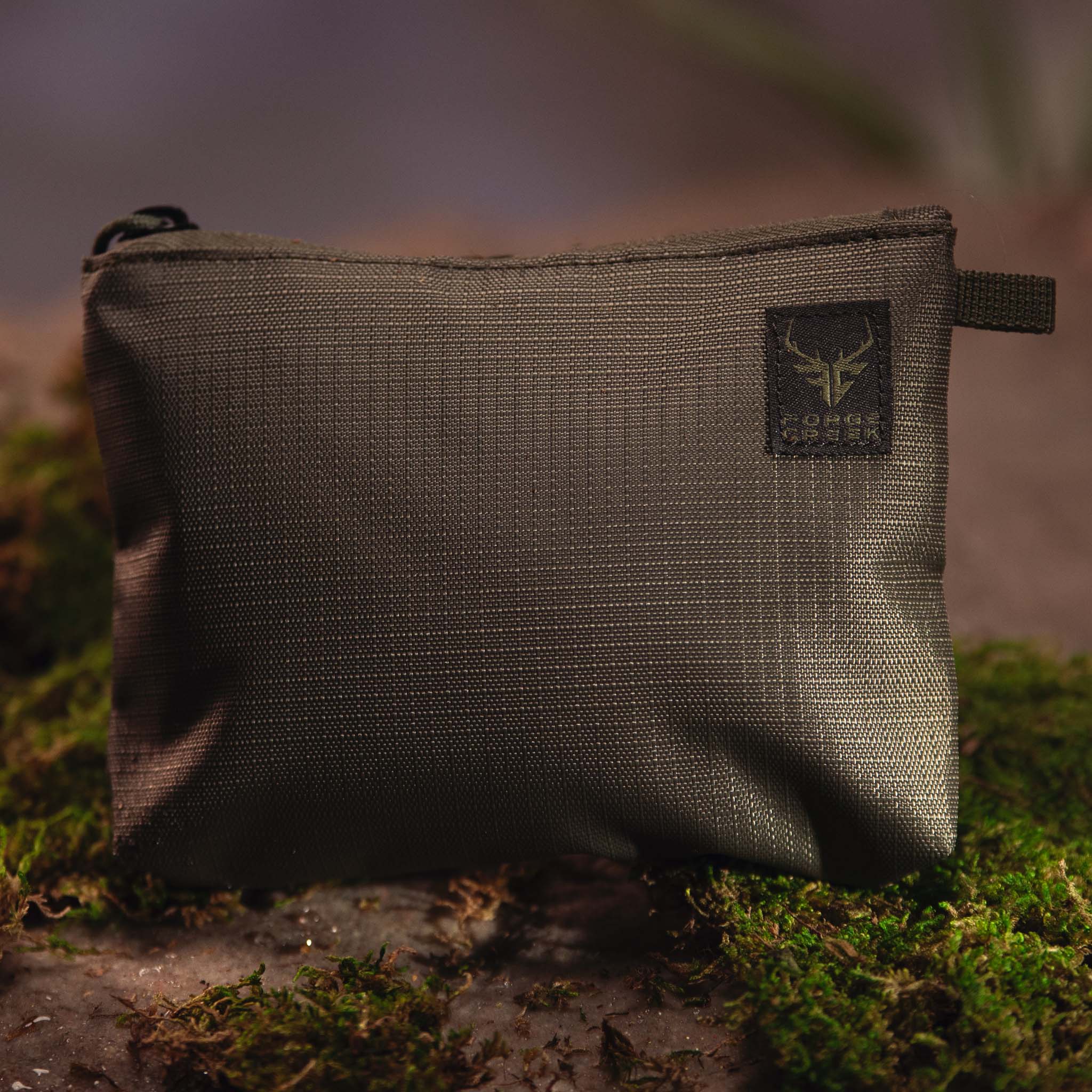 Olive green tactical pouch with Forge Creek logo, ideal for hunting gear storage on mossy forest ground
