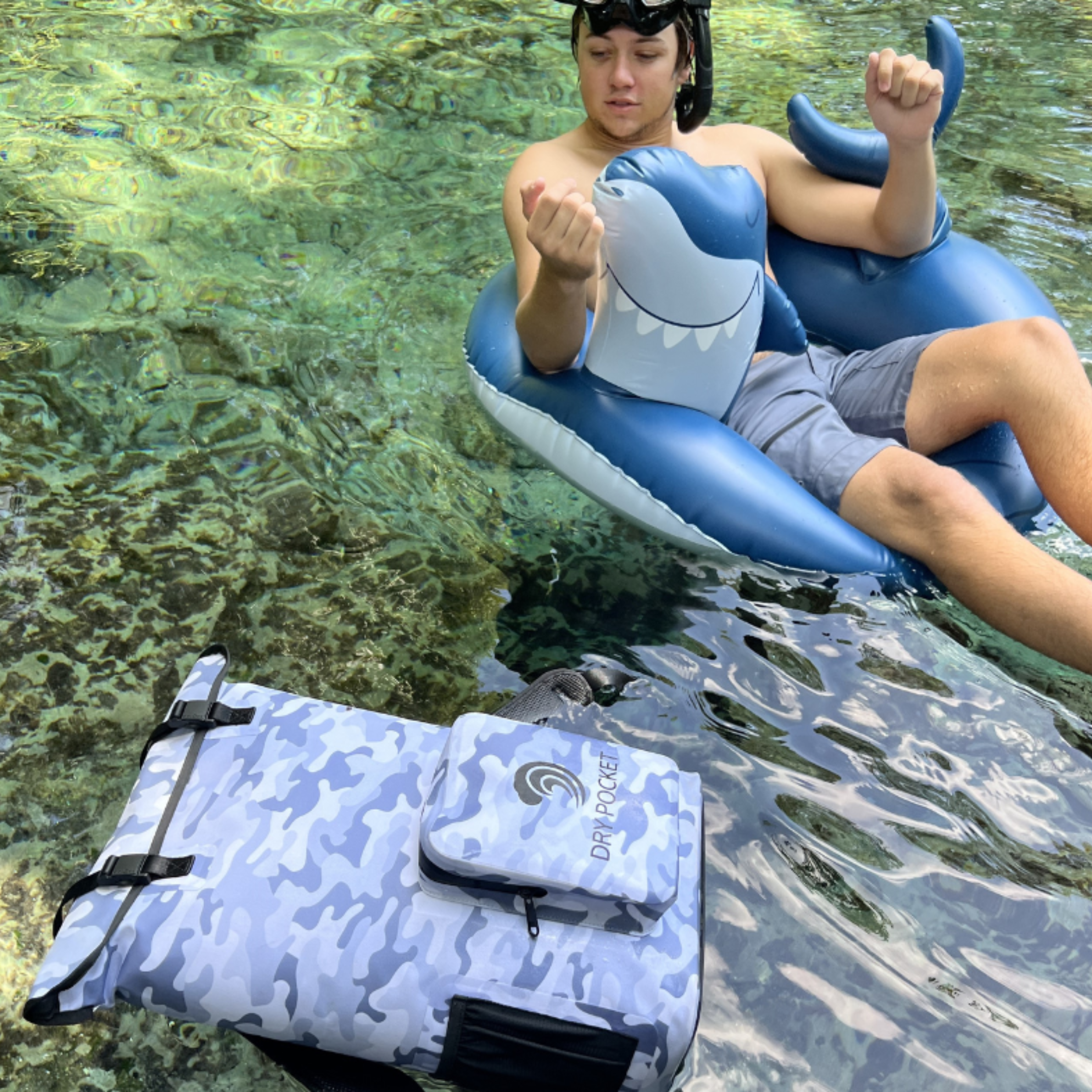 Blue camo dry bag and waterproof pouch floating in clear water with snorkeler on shark float
