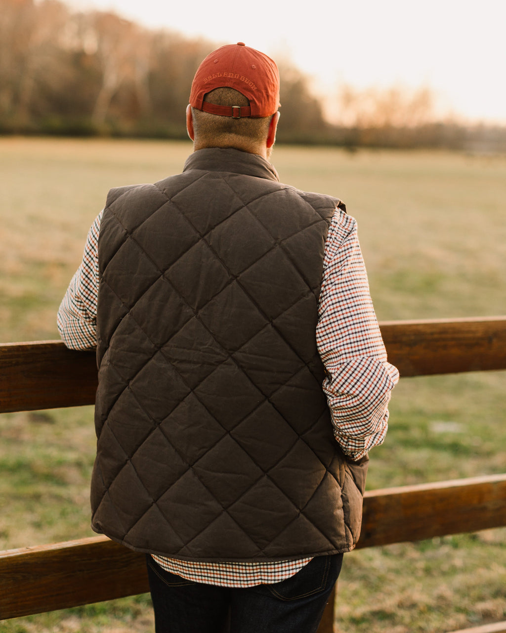 Brown Arthur Down Vest from behind at a split rail fence
