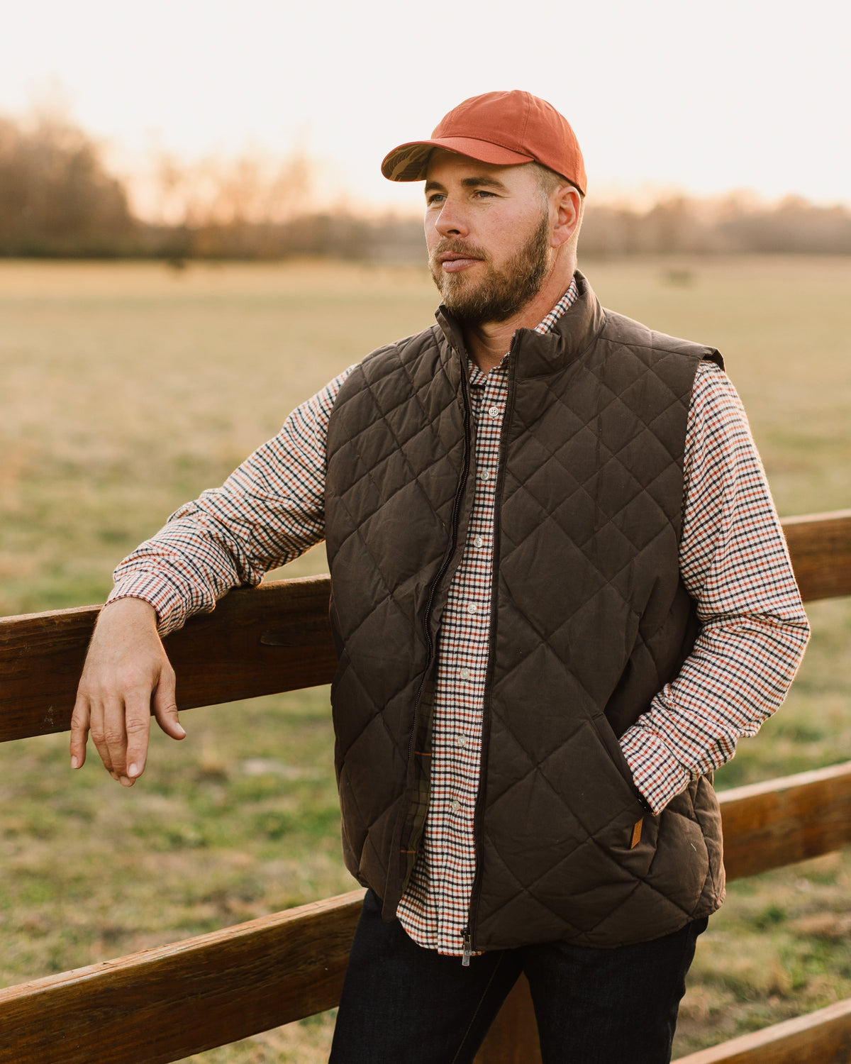Brown Arthur Down Vest worn leaning against a wooden fence
