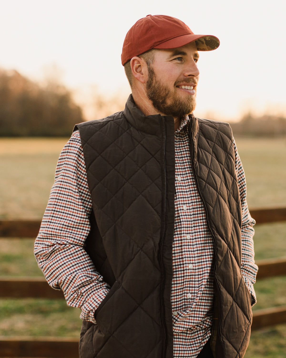 Man in a red cap wearing the Brown Arthur Quilted Waxed Down Vest over a check shirt