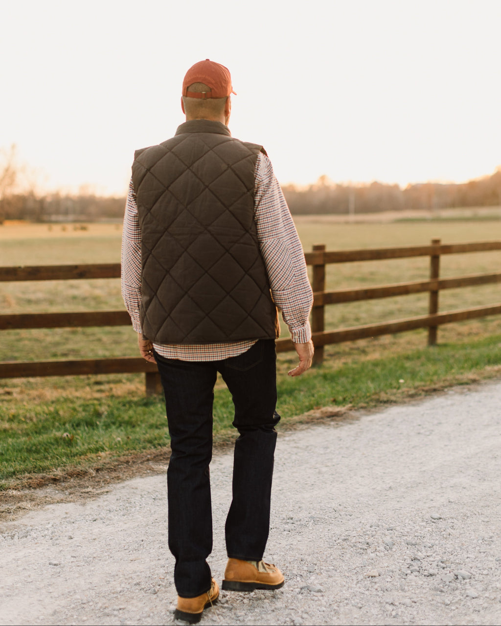 Back view of the Brown Arthur Down Vest worn on a gravel farm road