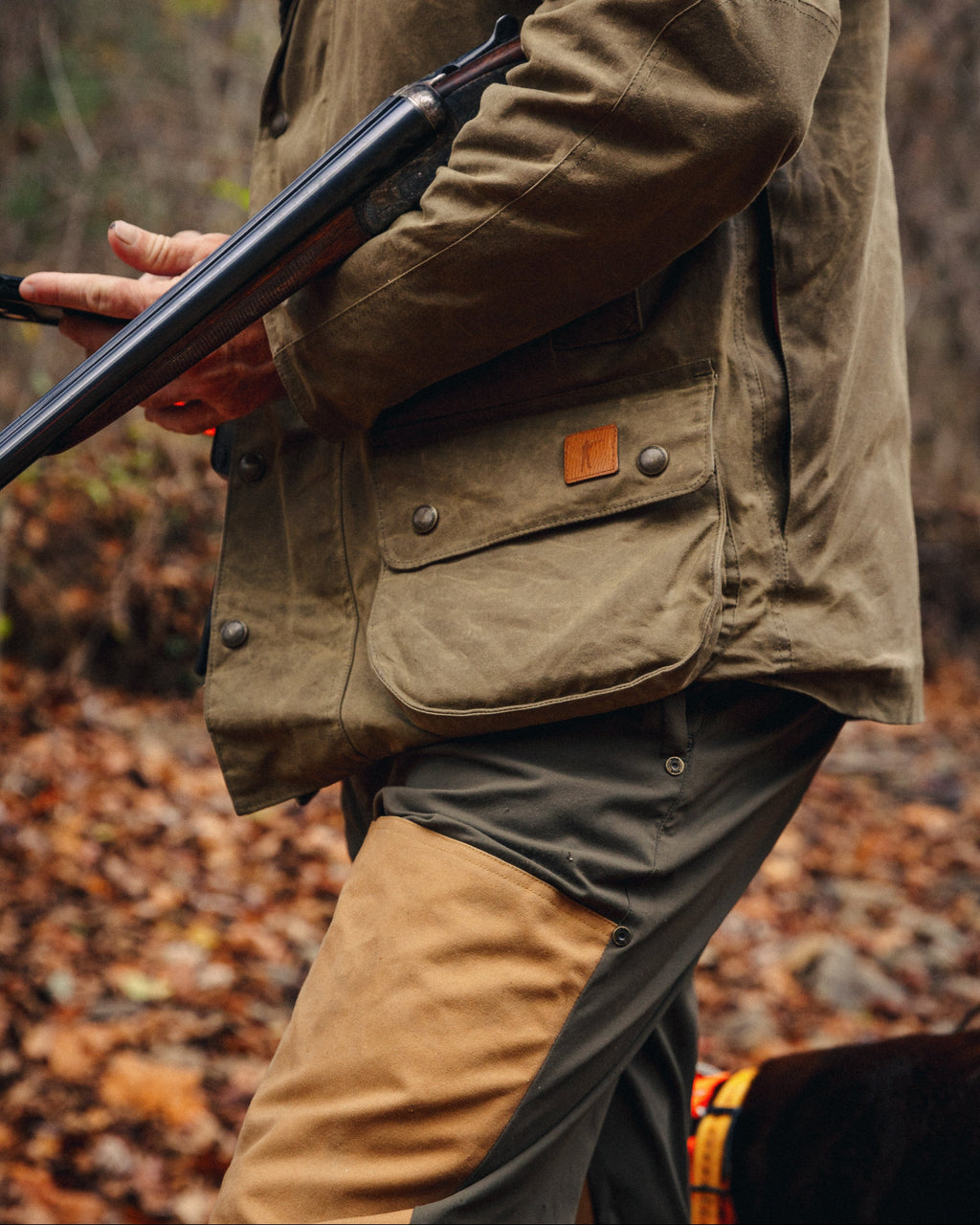 Upland Jacket worn with waxed field pants while holding a shotgun in fall leaves