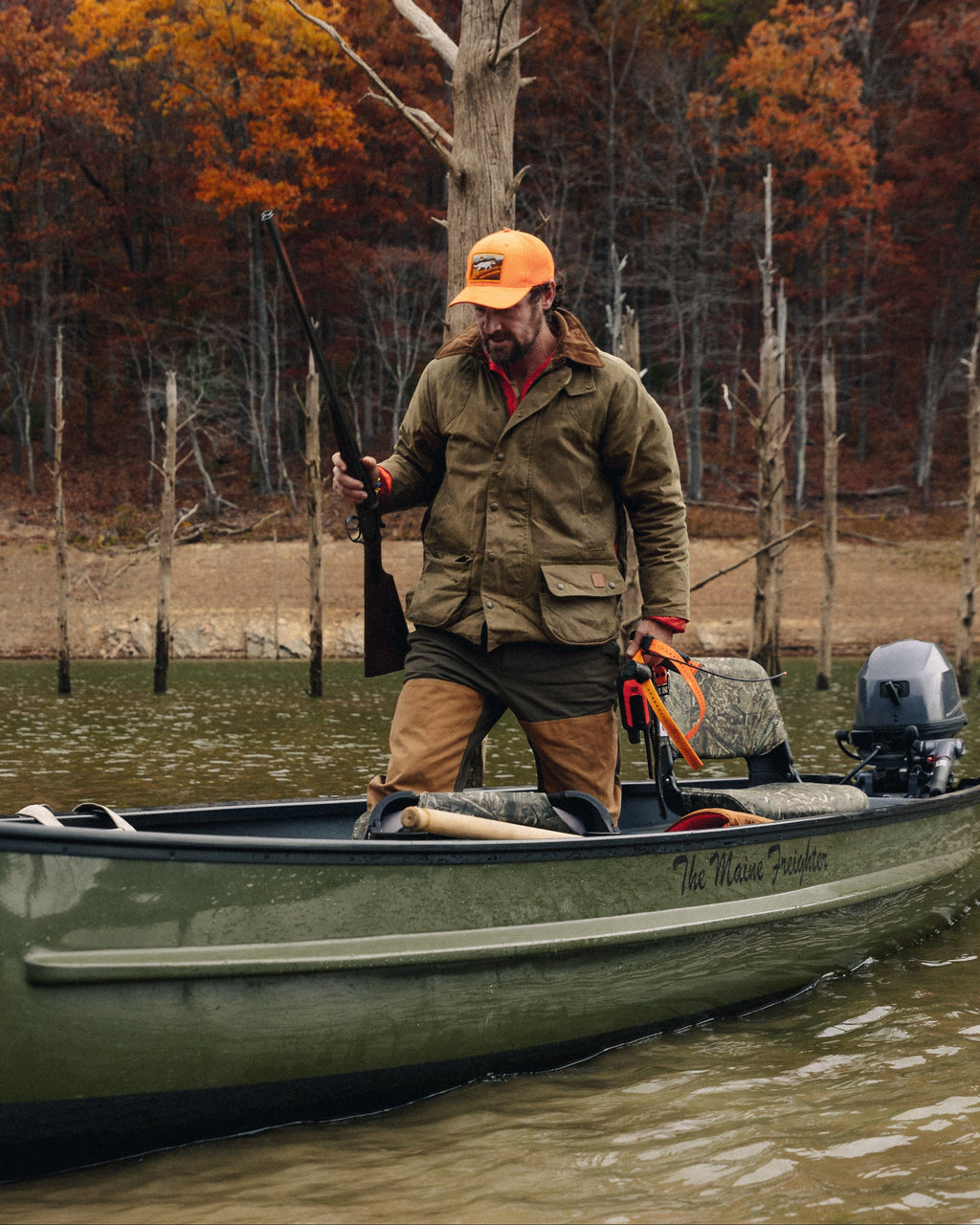 Hunter in a blaze orange cap and Upland Jacket standing in a jon boat in flooded timber