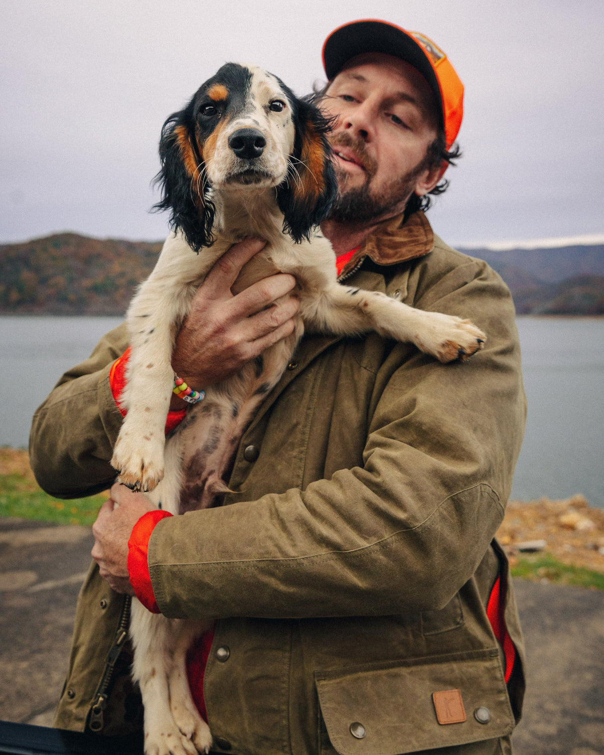 Hunter in a blaze orange cap and Upland Jacket holding a springer spaniel